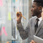 Two coworkers writing notes on a glass wall